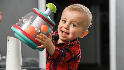 Junge im karierten Hemd hält strahlend ein Spielzeug nach oben